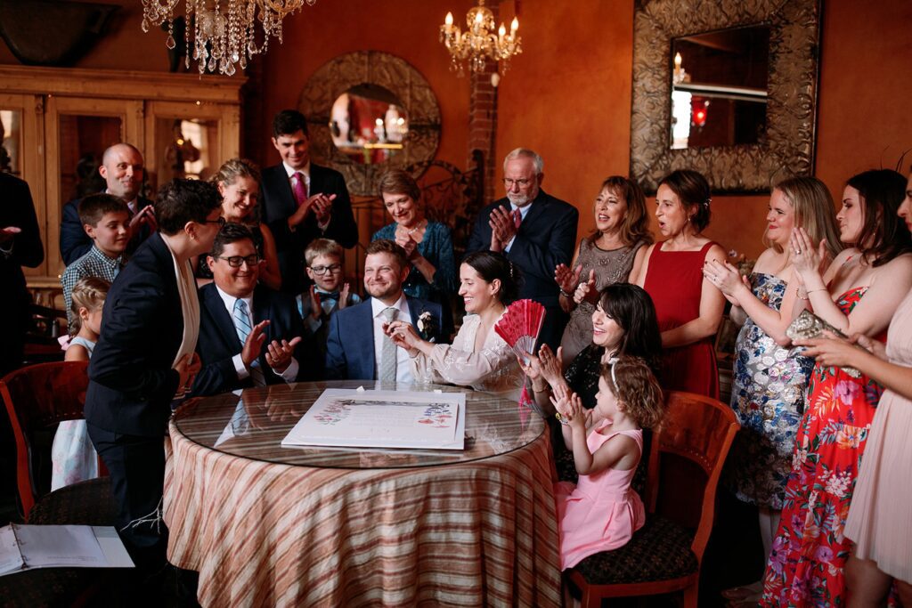 a family gathers around a table for a ketubah signing